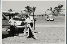 Members showing fishing equipment beside an airplane as golfers  practice on the adjacent golf course